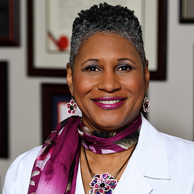 Sherita Golden, in a formal portrait, wearing a white lab coat and purple scarf